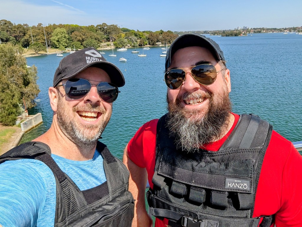 Joab Gilroy and Nathan Lawrence stand side by side wearing weighted vests. In the background is Iron Cove.