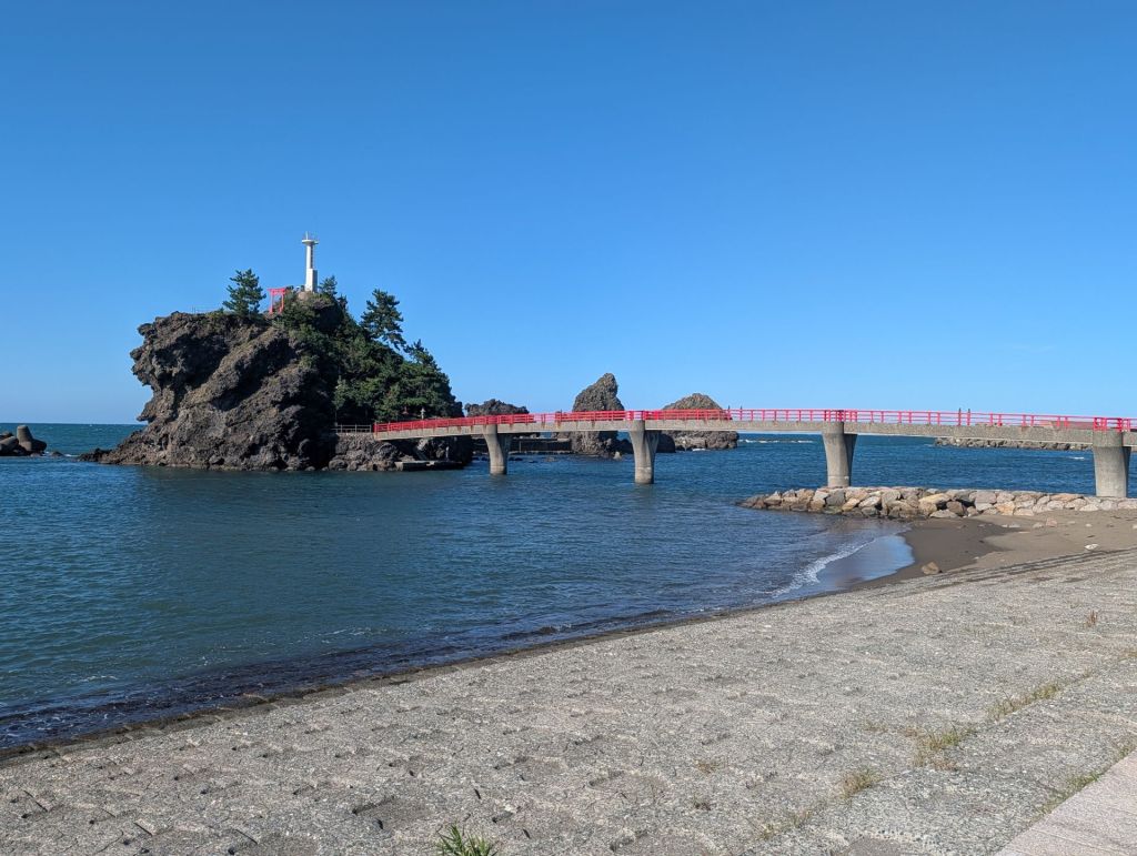 A red bridge creates a path to a rocky outcropping on the Sea of Japan.